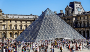 Gente contemplando el Louvre, una de las piramides de cristal mas importantes